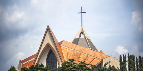 Modern church building with a cross on top and terracotta-tiled roof, surrounded by trees.