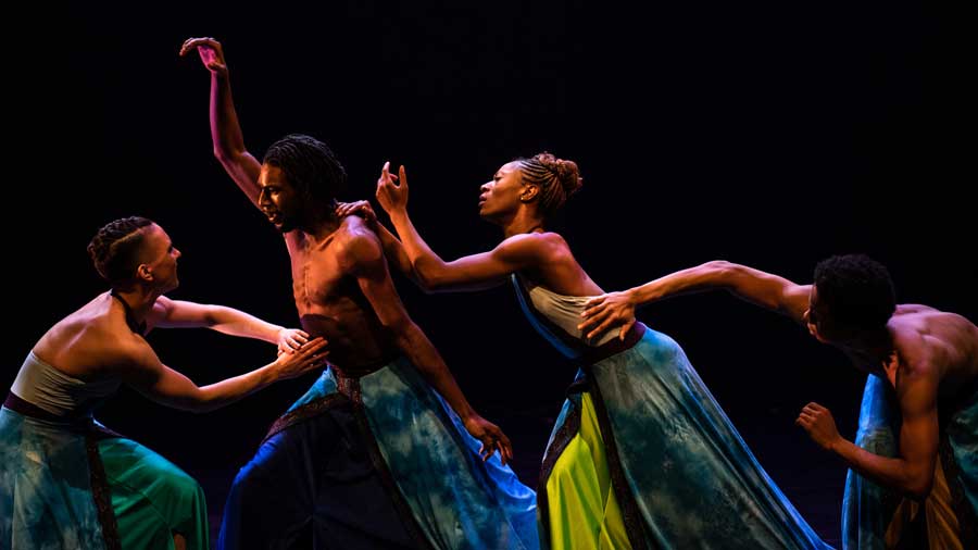 four professional dancers in motion, delicately touching each other with one hand