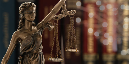 Bronze statue of Lady Justice holding scales, with blurred law books in the background