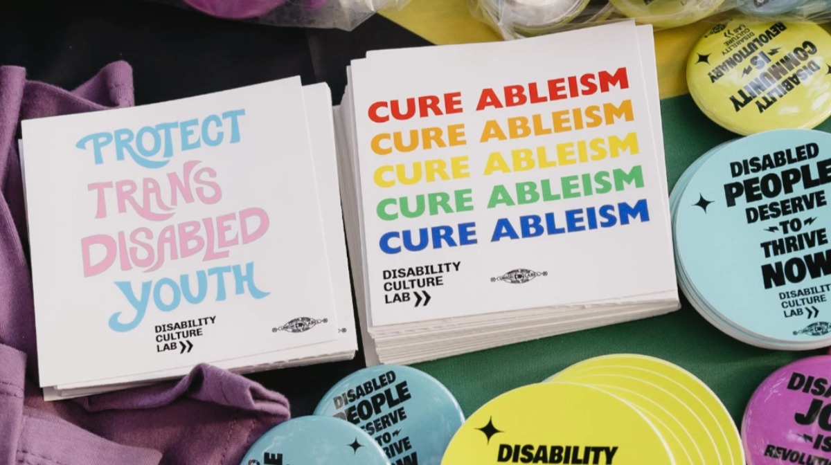 Stacks of stickers read “Protect Trans Disabled Youth” and “Cure Ableism” in various colors, advocating disability rights.